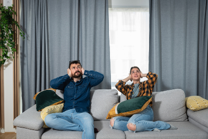 Couple sitting on the couch covering their ears